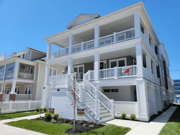 Modern white three-story beach house with multiple balconies and white railings under blue skies.